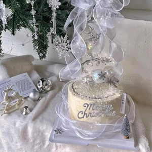 White Christmas tree cake topper decoration set with ribbons and ornaments for holiday party.