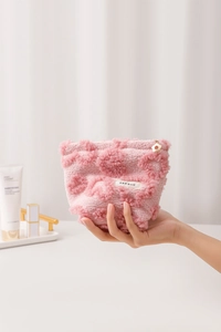 Trousse de maquillage en peluche rose avec texture cœur tenue en main pour voir la taille