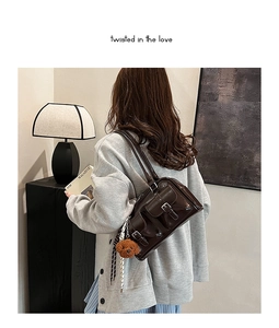 Detail of dark brown leather shoulder bag with side pockets and a plush bear charm