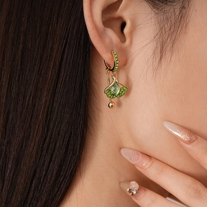 Close-up of gold fan-shaped earrings with green crystals worn by a model