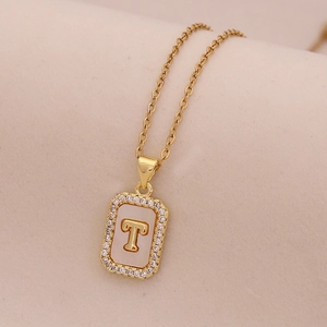 Vue macro du collier doré 18K avec pendentif lettre T, nacre et petits cristaux