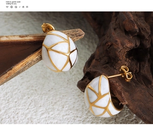 Macro shot of white enamel stud earrings with gold geometric lines on vintage wood texture