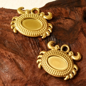 Macro shot of two gold 18K plated stainless steel crab charms with oval inlay details