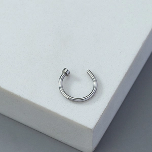 Detail of silver non-pierced nose ring with round disc end on white marble pedestal
