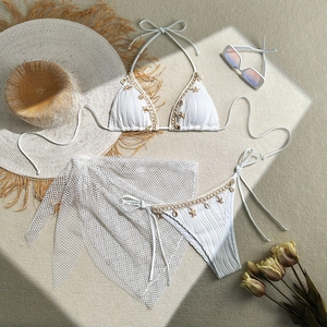 Detail of white bikini with starfish metal chains and mesh sarong on a sandy fabric
