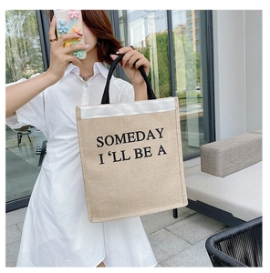 Outdoor shot of a beige canvas tote bag with black handles and white top panel details