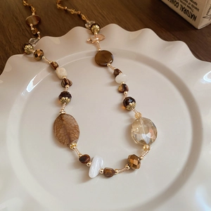 Dettaglio della collana di perle marroni e agata stile Maillard su un piatto di ceramica