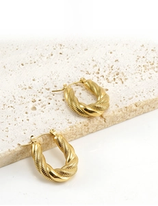 Detail of 18K gold plated twisted hoop earrings on a textured stone platform