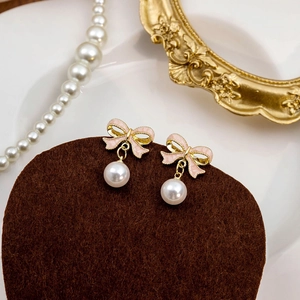 Detailed view of pink bow earrings with white pearl pendants on a velvet display