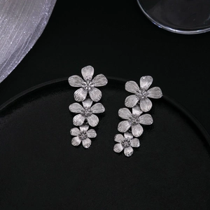 Detailed view of silver metallic triple flower drop earrings on a black textured surface