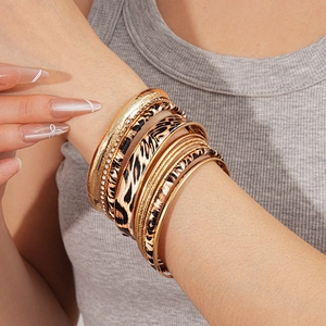Close-up of leopard print metal bangles layered with crystal accents on a grey knit sleeve