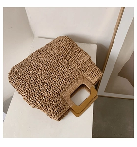 Detail showing natural straw fiber texture and rectangular wooden handle on the tote bag