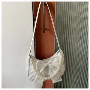 Detail of white lace shoulder bag featuring a large satin bow and pearl chain strap