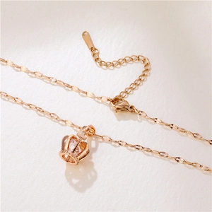 Collier élégant en or rose avec pendentif couronne et zircon sur fond texturé beige