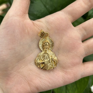 Detail of a gold Saint Jude pendant held in hand with natural green leaf background