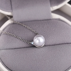 Macro shot of elegant white pearl pendant necklace with sparkling cat ear detail on velvet