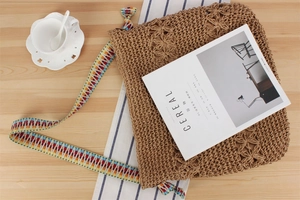 Detail of hand-woven straw tote bag with colorful geometric strap on wooden desk