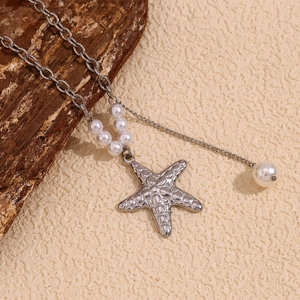 Close-up of silver starfish pendant with white pearls on a chain over sand