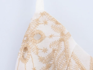 Macro detail of intricate gold embroidery and hollow-out patterns on cream cotton linen
