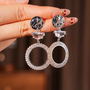 Detailed close-up of crescent hoop earring with textured disc and shimmering crystals
