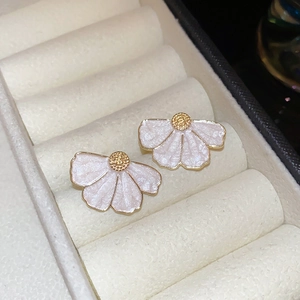 Vue macro de boucles d'oreilles fleurs en émail blanc avec placage or sur tissu blanc