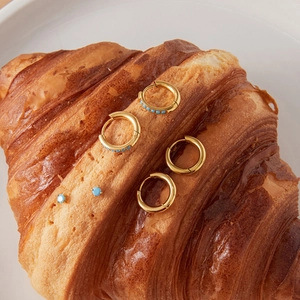 Makroaufnahme von goldenen Edelstahl-Ohrringen mit Türkissteinen auf einem Croissant