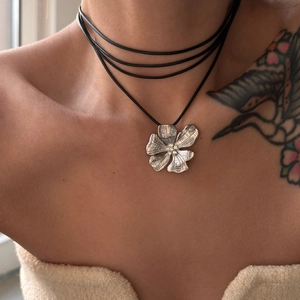 Macro detail of silver flower pendant with rhinestones on multi-layer black cord necklace