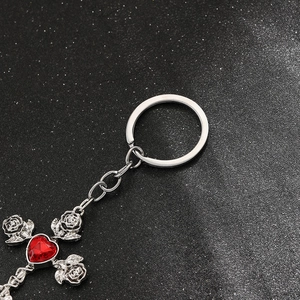 Close-up of gothic silver cross keychain with red heart gemstone and rose details