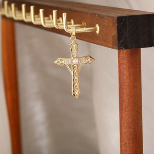Dettaglio ravvicinato di un ciondolo a croce d'oro con zirconi su un supporto in legno