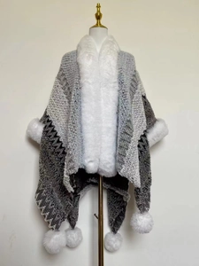 Close-up of ethnic knit shawl with faux fur collar and decorative white fur pom-poms