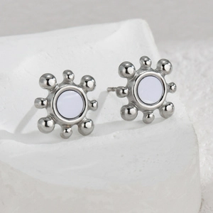 Minimalist silver sunburst stud earrings with white center on textured background