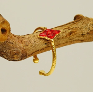 Detail of red zircon flower open bangle on wood stand with hammered gold texture