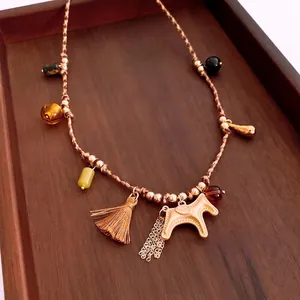 Ethno style woven rope necklace with a horse pendant and metal tassels on wooden tray