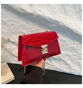 Detail of red crossbody bag with crocodile pattern flap and golden metal chain link