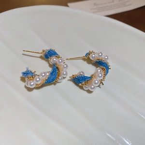 Close-up of C-shaped earrings with blue denim fabric, white pearls, and gold wire wrap