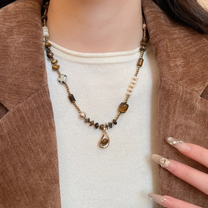 Close-up of tiger eye stone necklace with gold teardrop pendant on female model