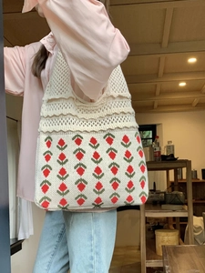 Detail of hand-knit cream tote bag featuring red strawberry jacquard and floral lace design