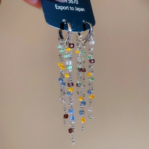 Detail of heart-shaped earrings with colorful crystal tassels and silver metal chains