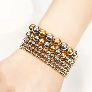 Detailed view of layered gold and silver stainless steel bead bracelets on wrist