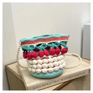 Detail of crochet bucket bag with cherry accents and elegant faux pearl shoulder strap