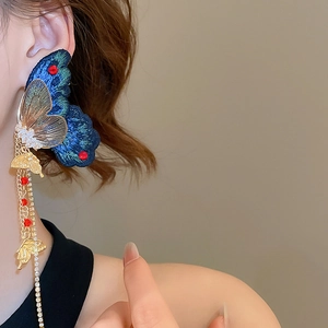 Détail de boucle d'oreille papillon brodée bleue avec franges dorées sur un modèle