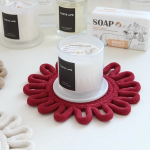 Close-up of white soy wax candle on deep red flower shaped woven cotton coaster