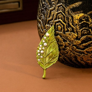 Close-up of green leaf brooch featuring multiple pearls on a vintage background