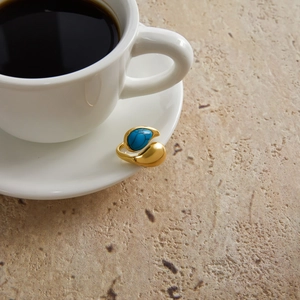 Detail of a gold titanium steel ring with a textured blue natural stone on a white saucer