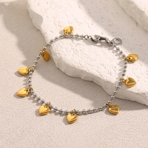 Detailed view of beaded silver bracelet with multiple golden heart charms on stone surface