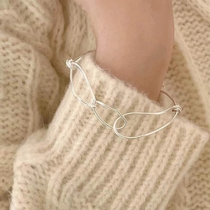 Detailed close-up of a silver knot woven bangle on a wrist with a beige knit sweater