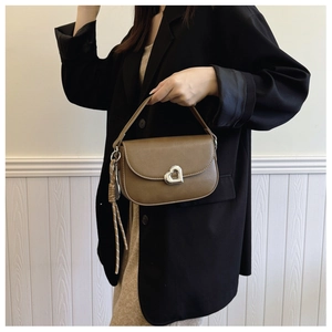 Detail of a brown leather saddle bag featuring a silver heart-shaped metal buckle