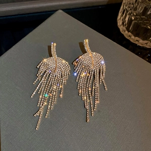 Close-up of sparkling rhinestone leaf tassel earrings with golden finish on dark fabric