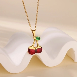 Sweet red cherry pendant necklace with gold chain on a white decorative stand