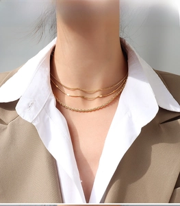 Detail of layered 18K gold plated titanium steel necklaces worn by a model in a suit